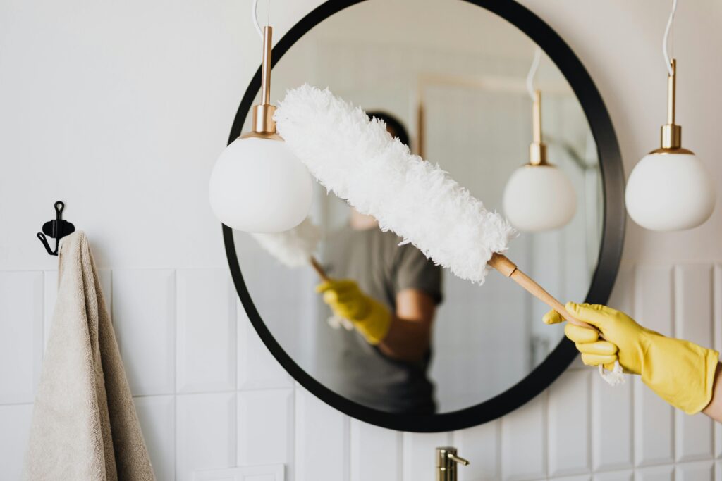 Gloved hands dusting an elegant bathroom mirror to help reduce dust in home spaces