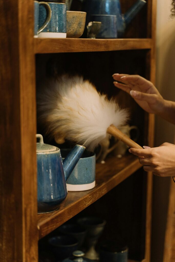 Hands cleaning pottery on a wooden shelf to help reduce dust in home spaces